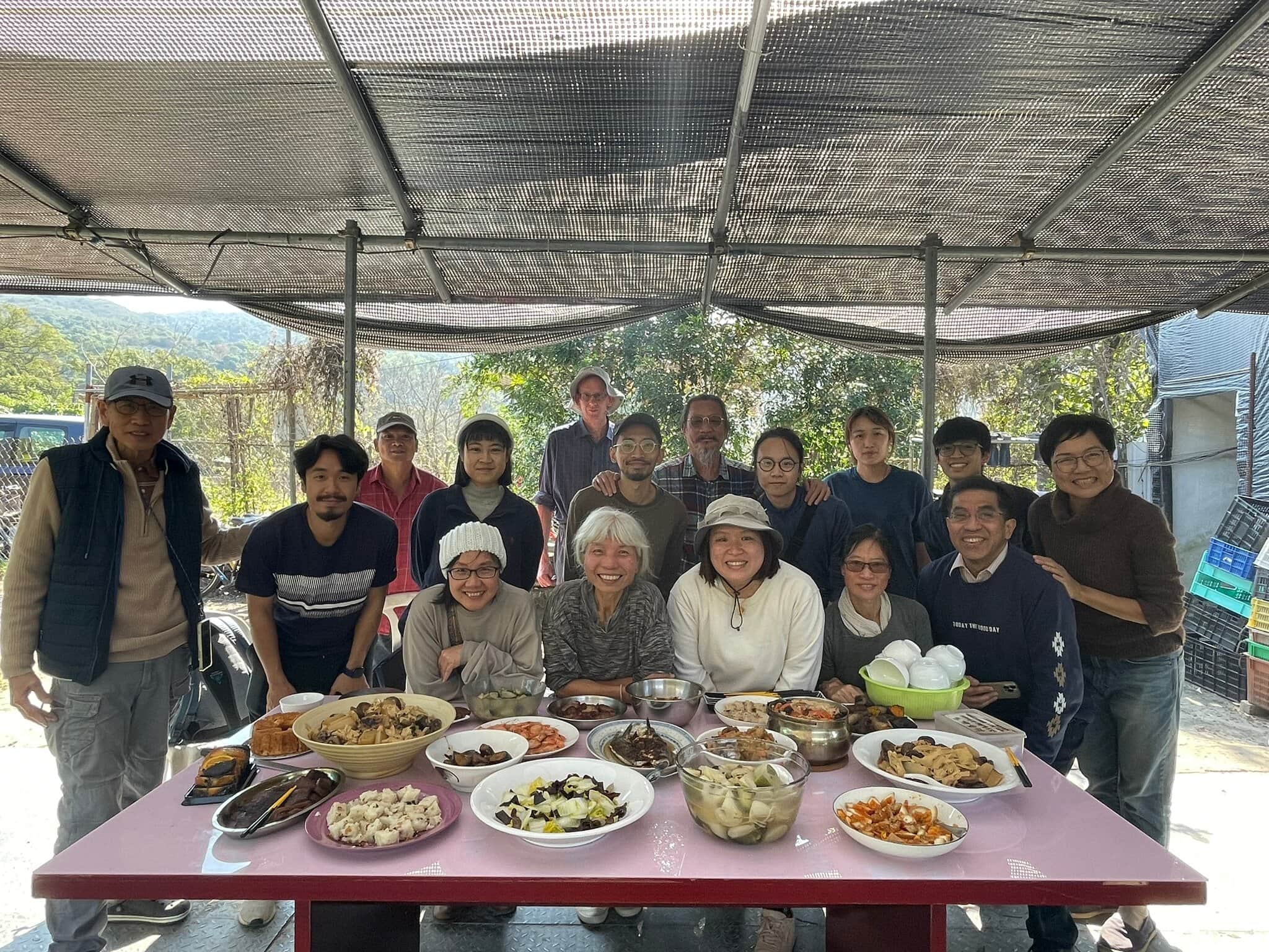Group of people around a table with various dishes under a canopy.