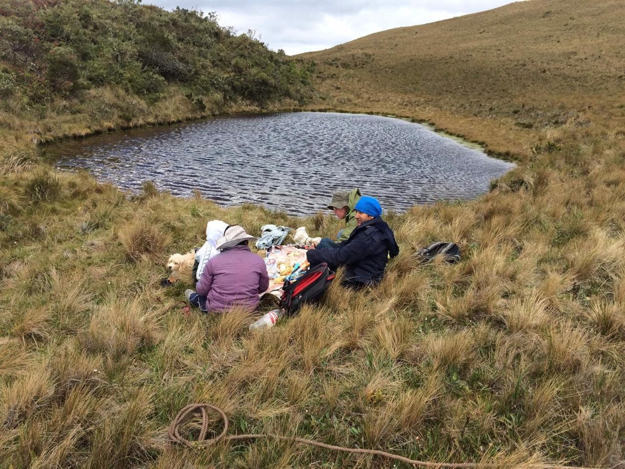 Group of people near a small lake at a grassy field with hills.