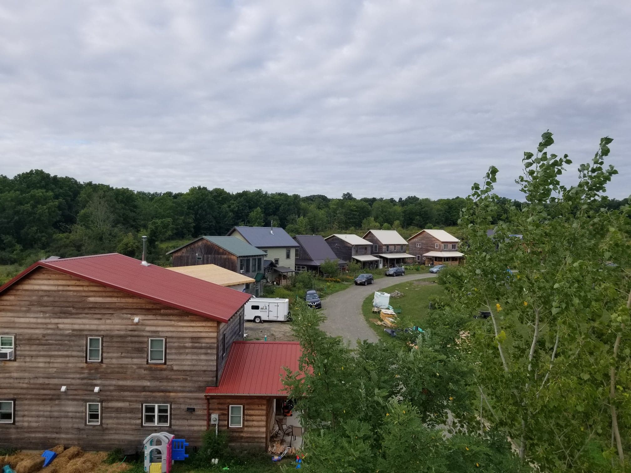 Aerial view of timber eco-homes in a village setting with lush trees and a gravel road.
