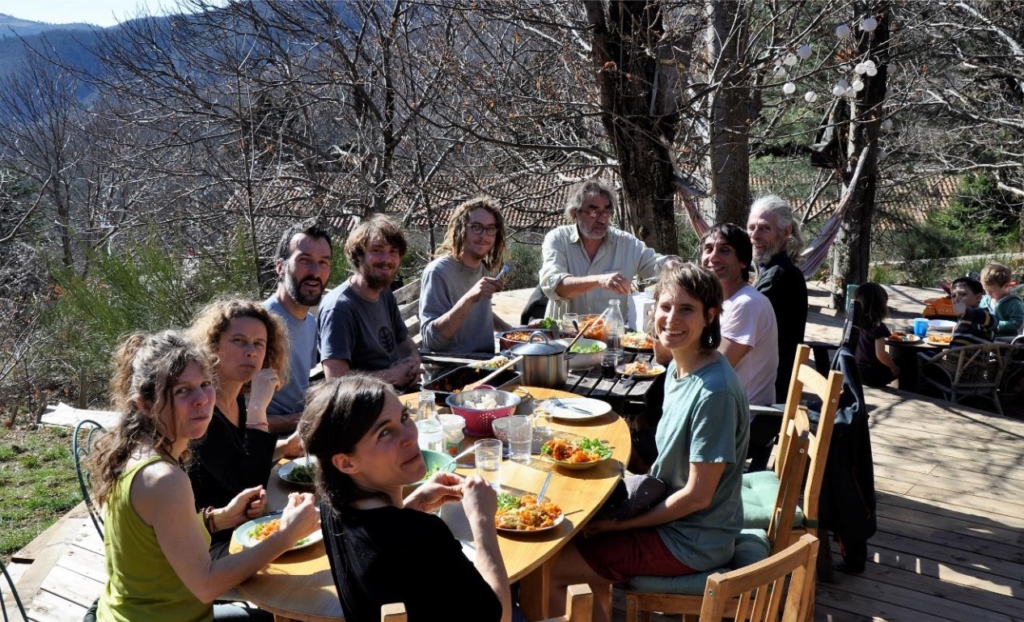 Group of people sharing a meal on an outdoor wooden deck in a woodland setting.