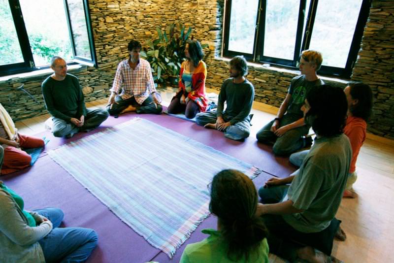 Participants seated in a circle on a purple rug inside a stone-walled room.