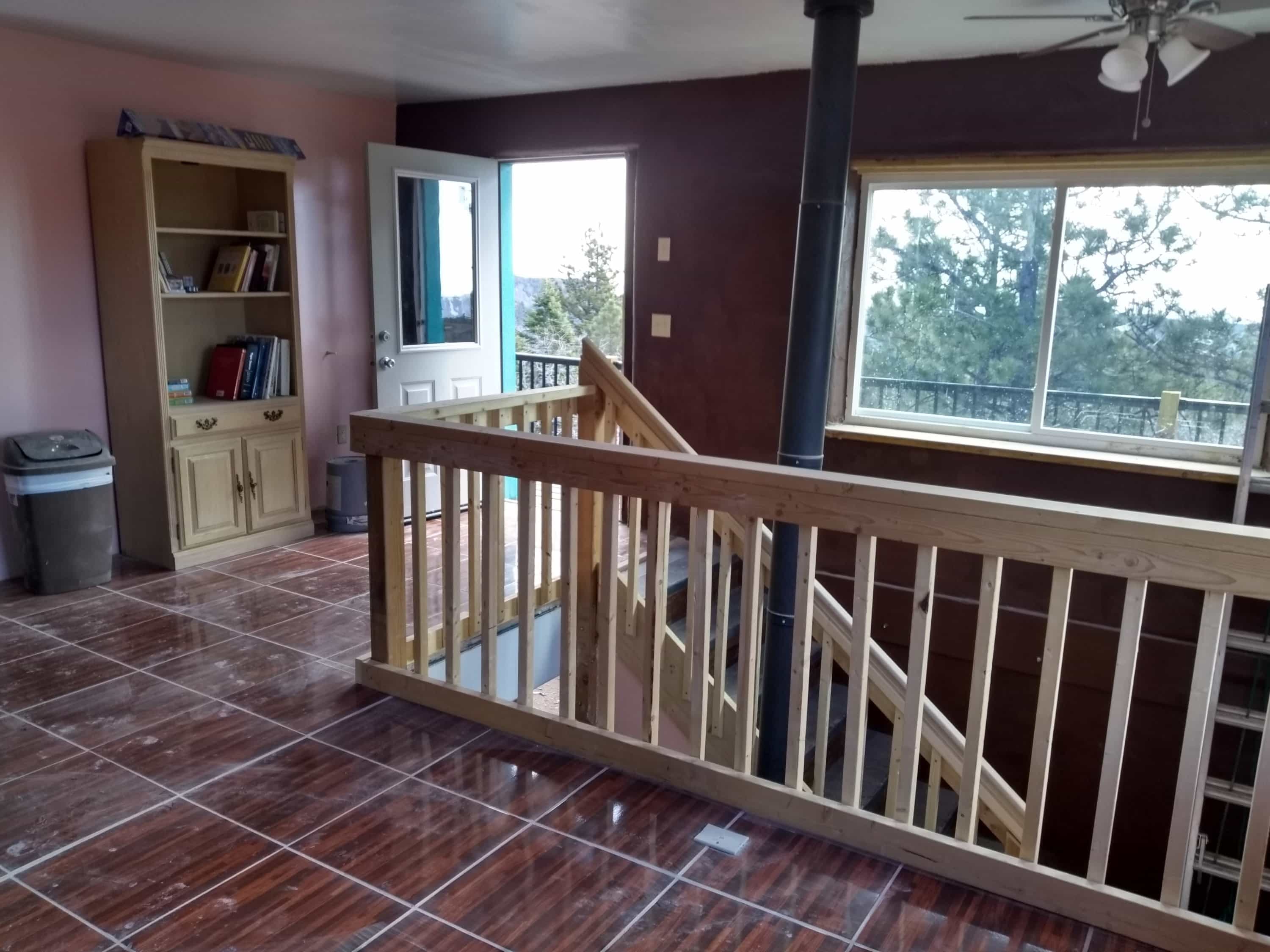 Inside space with wooden railing and stairwell overlooking the outdoors.