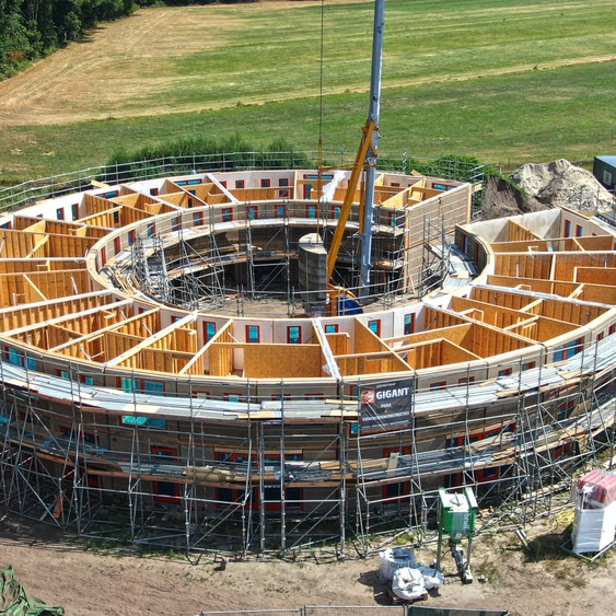 Circular wooden eco-village under construction with scaffolding and crane.