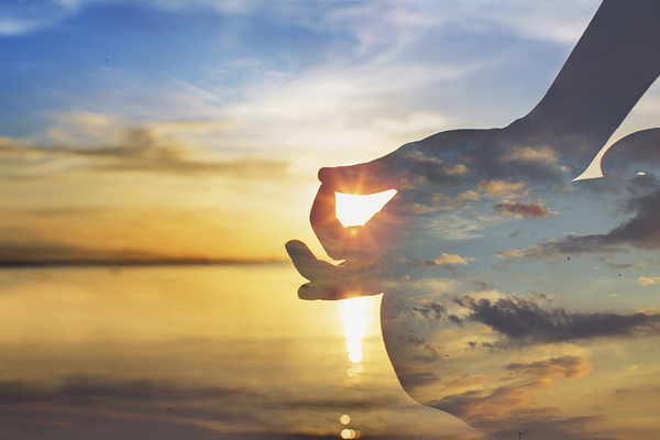 Sunset over water with silhouette of hands forming a mudra.
