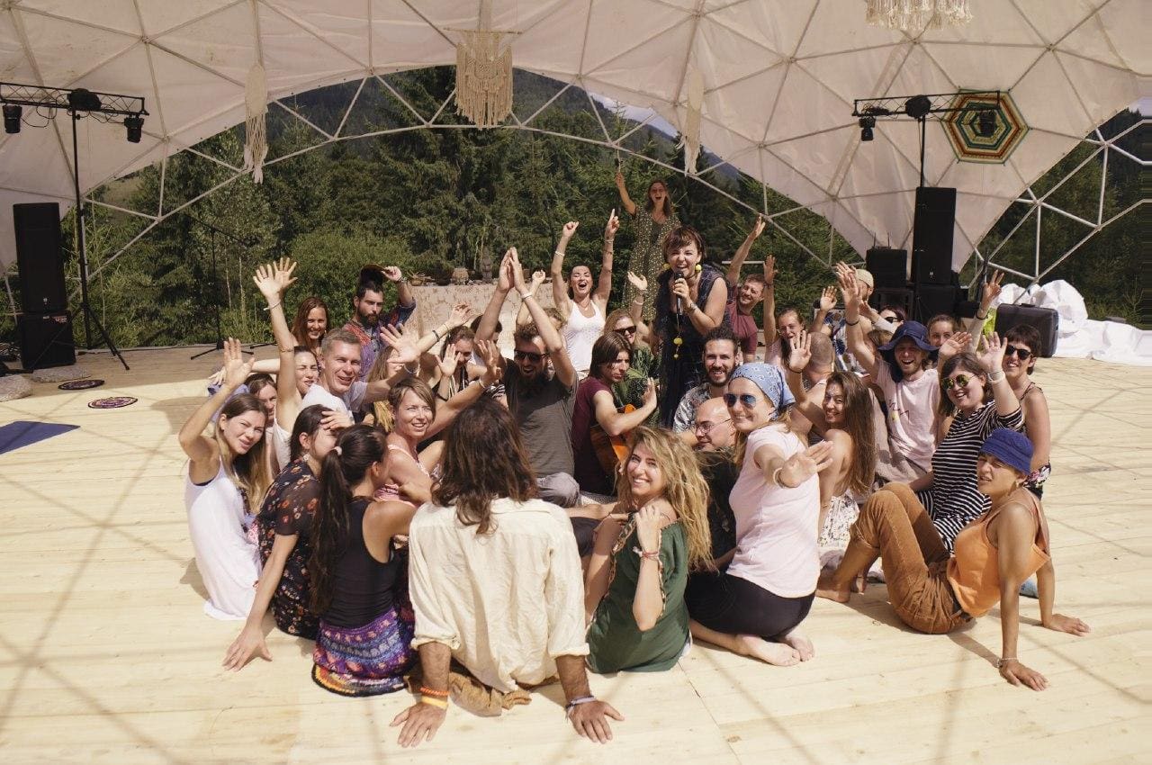 Group of people at an eco village event raising hands under a canopy stage.