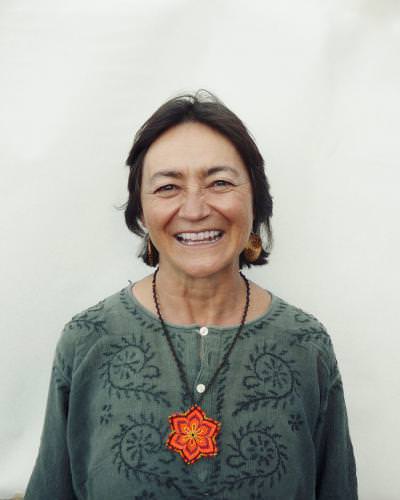 Portrait of Beatriz Arjona smiling wearing a green embroidered top and a red flower pendant.