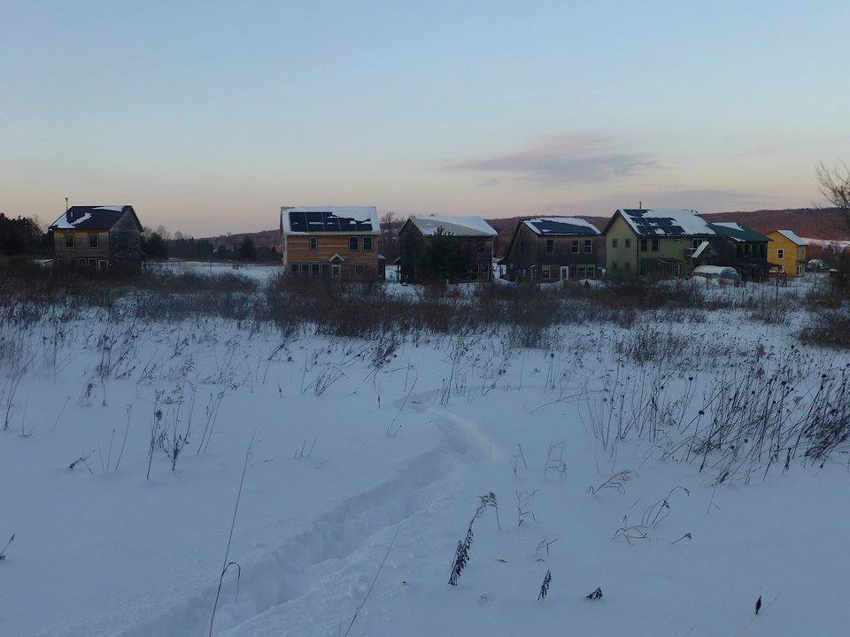 Snow-covered eco-village houses lined up along a open field at dawn.