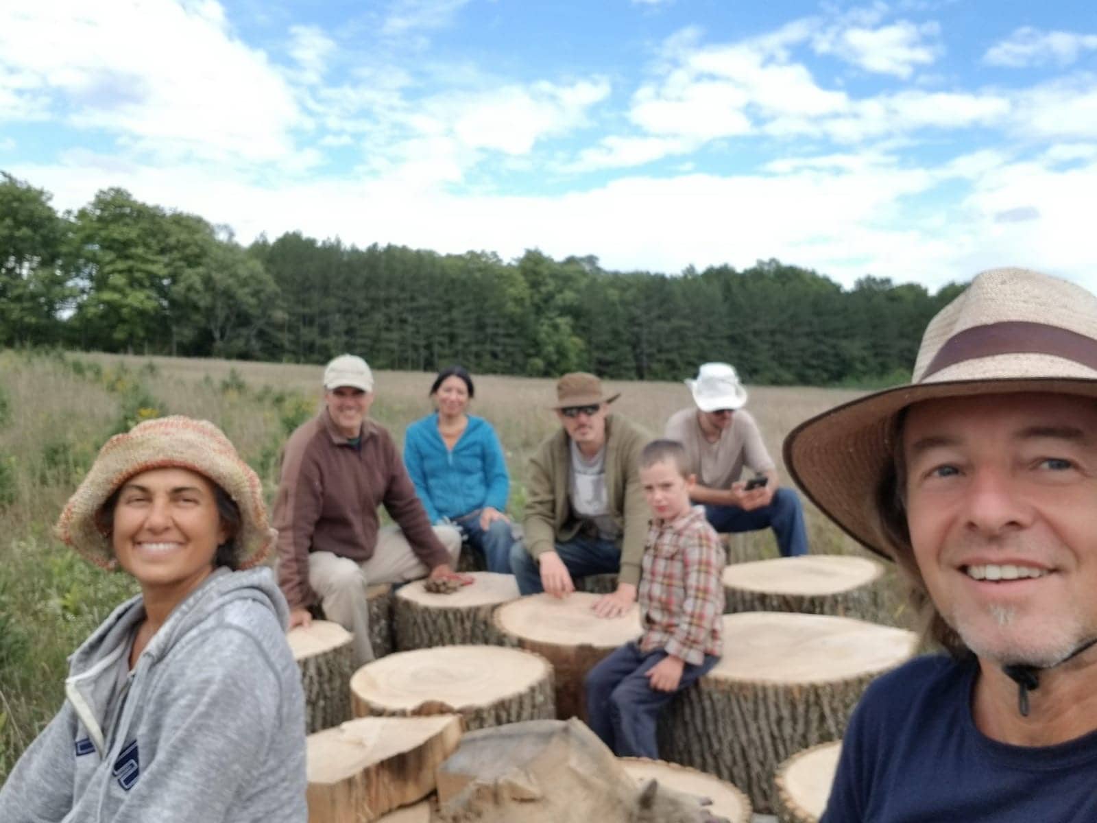 Group of people outdoors in a field with tree stumps used as seating.