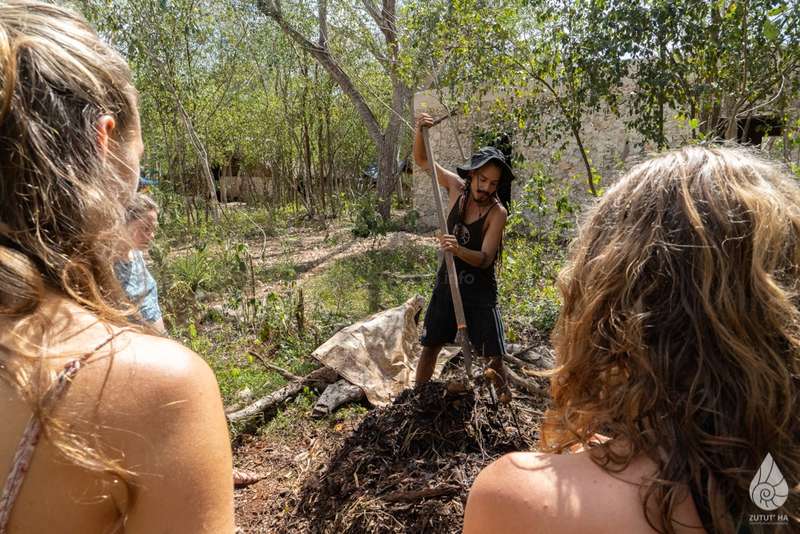 Person digging with a shovel among trees in an eco village setting.