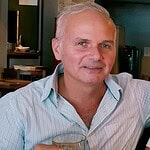 A smiling man in a light blue shirt in a cafe setting.