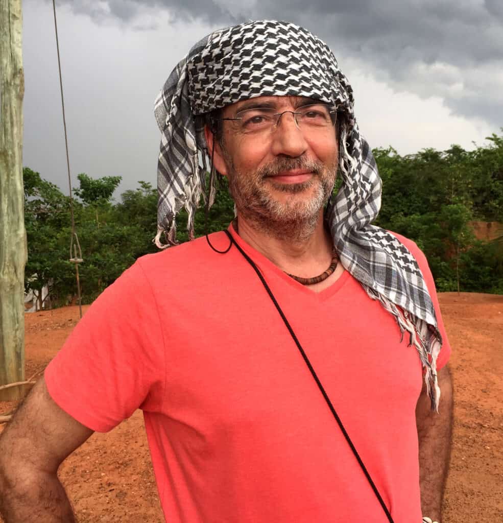 Man wearing pink t-shirt with keffiyeh scarf outdoors.