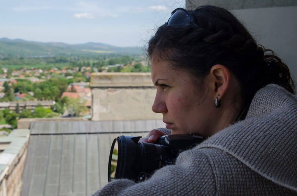 Female photographer capturing scenic view from rooftop in a rural village setting.