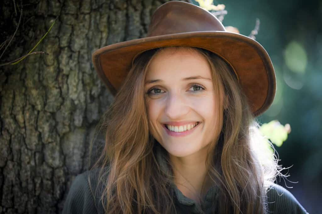 Smiling young woman wearing a hat in a natural outdoor environment.