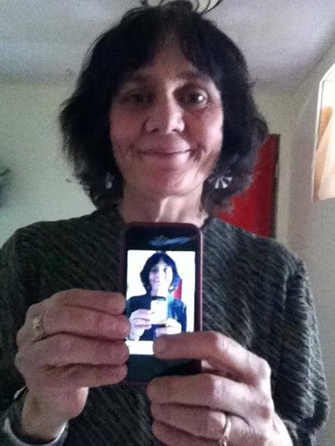 Portrait of Linda Joseph holding a phone with a reflection.