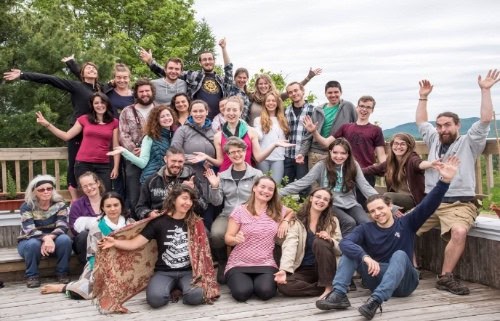 Group of diverse people smiling and raising hands on a wooden deck.