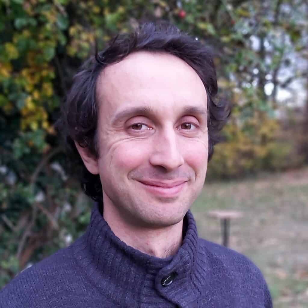Portrait of a smiling man outdoors with greenery in the background.