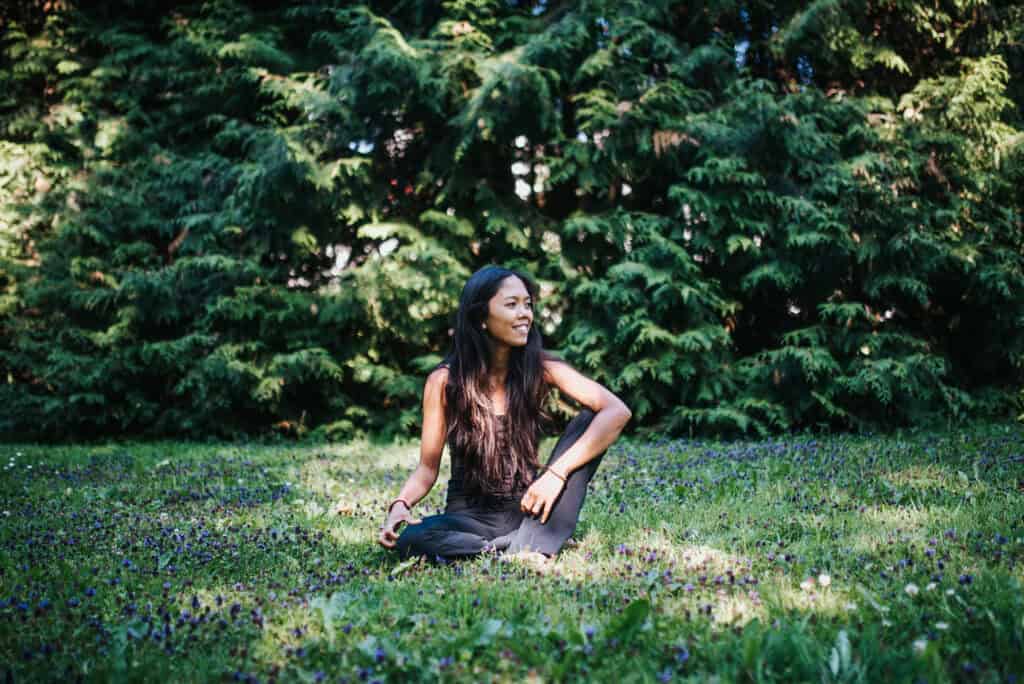 Woman sitting cross-legged on meadow among wildflowers with trees in background.