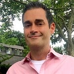 Portrait of a man in pink shirt outdoors with trees in background.
