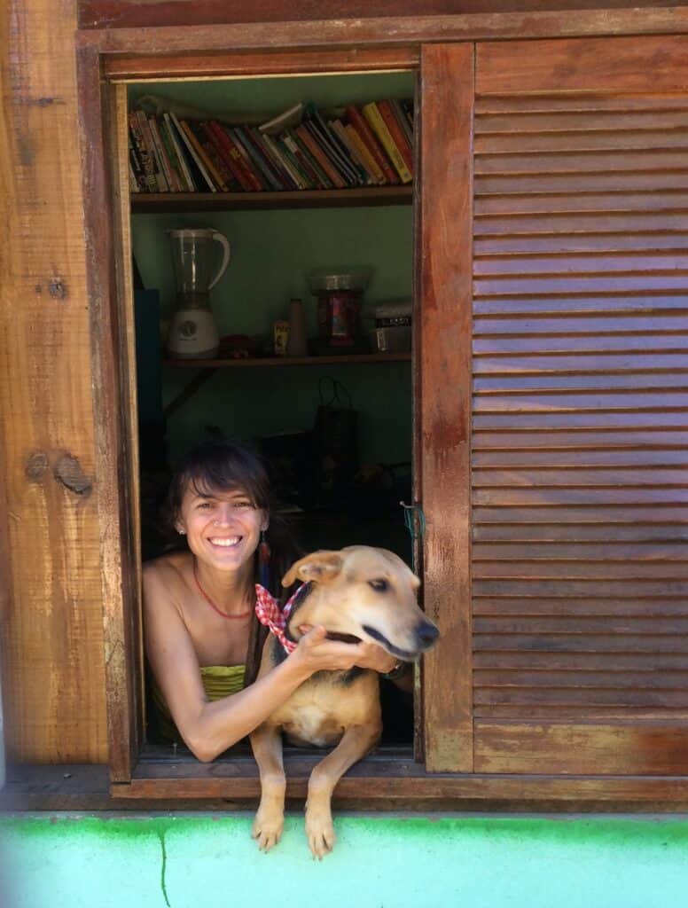 Woman smiling with a dog at a wooden doorway, EcoVillage setting.