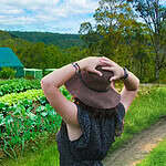 Person in a hat standing beside lush vegetable beds at EcoVillage garden.