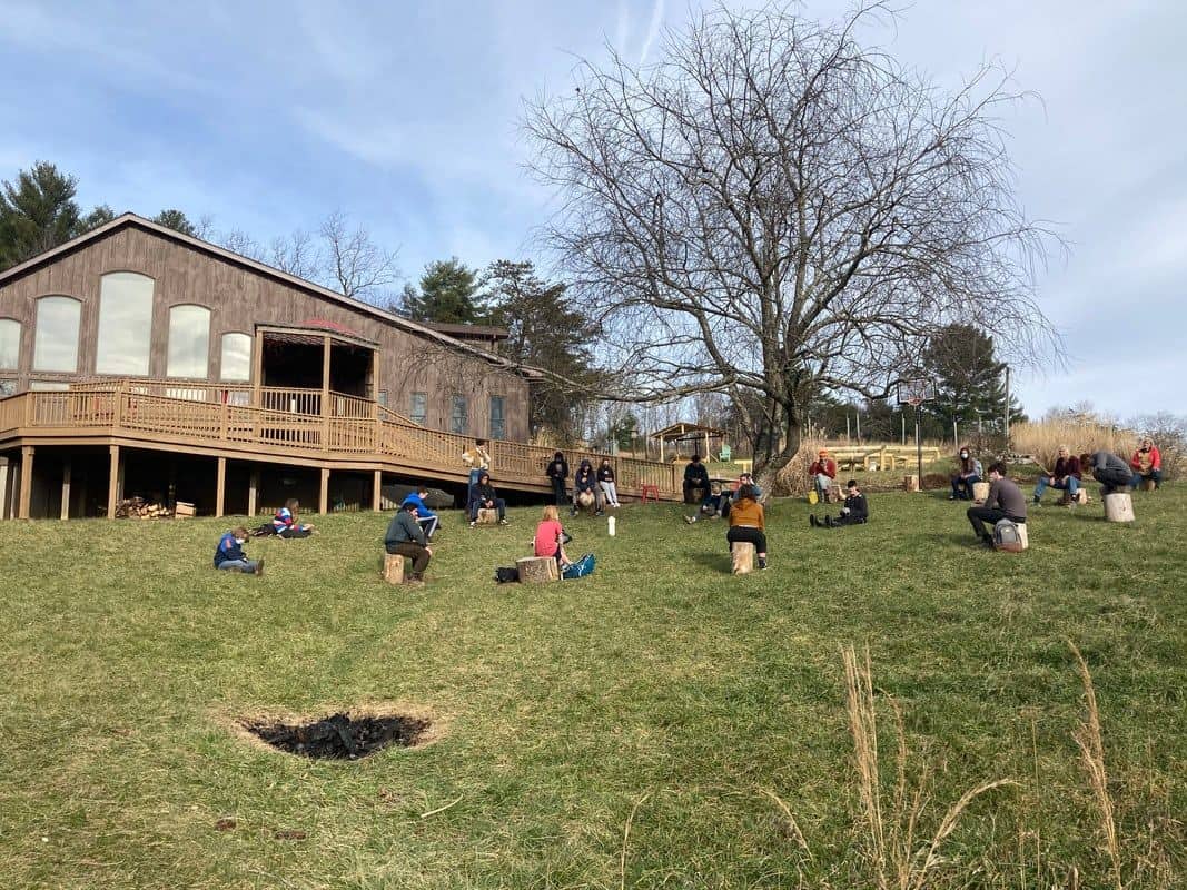 Group of people outdoors at an ecovillage gathering near a wooden building.
