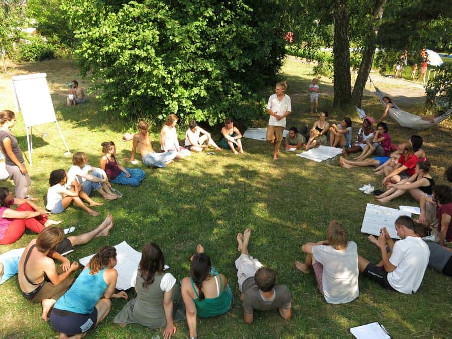 People seated in a circle in a green park for a community gathering.
