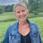 Smiling woman in denim jacket outdoors in green field.