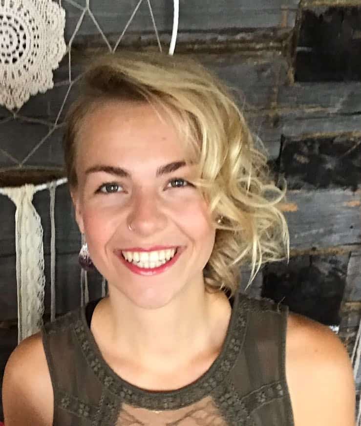 Smiling woman with short blond hair in rustic setting, eco-friendly vibe.
