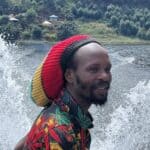 Person with colorful dreadlocks by a lake in a tropical setting.