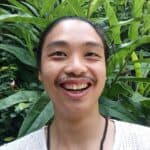 Smiling person in front of lush green plants, Asia-inspired wellness vibe.
