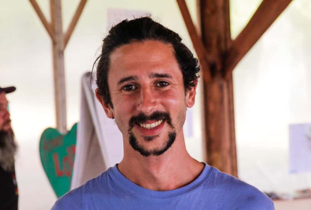 Man smiling in a casual blue shirt at an eco village event.