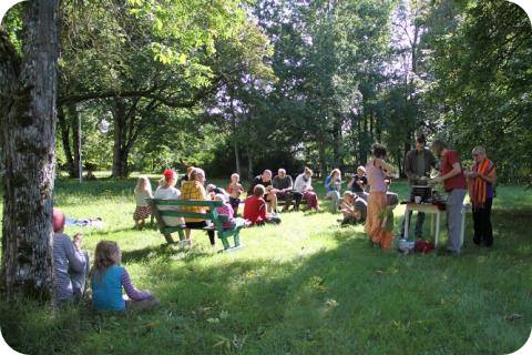 Group of people outdoors in a park, meeting around a sunny grassy area with trees.