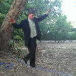 Man in a suit balancing on a blue line outdoors, nature background.