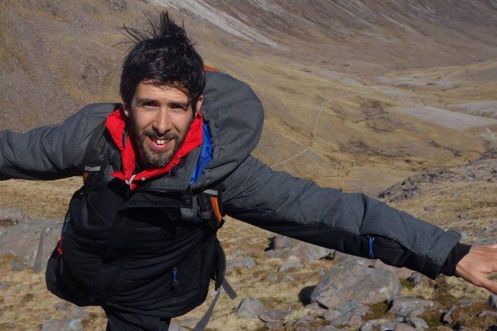 Person climbing on rugged mountain terrain with arms outstretched.