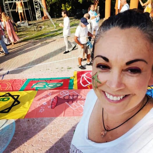Smiling woman at outdoor ecovillage event with colorful banners.