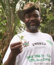 Man in a white T-shirt holding a small plant in a garden.