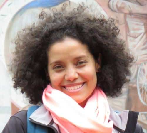 Smiling woman with curly hair, pink scarf in an outdoor setting.