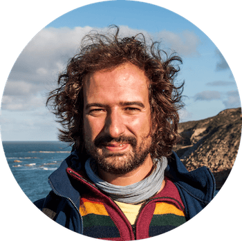 Portrait of a man with wavy hair and beard by the coast.