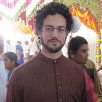 Portrait of a man in a brown kurta at an event with colorful decorations.