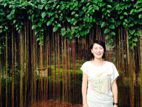 Woman standing in front of hanging vines in a lush garden setting.