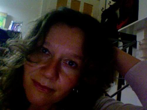 Portrait of a woman with wavy hair, relaxed smile, indoor setting.
