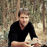 Man outdoors with wooden craft model in forest seedlings.