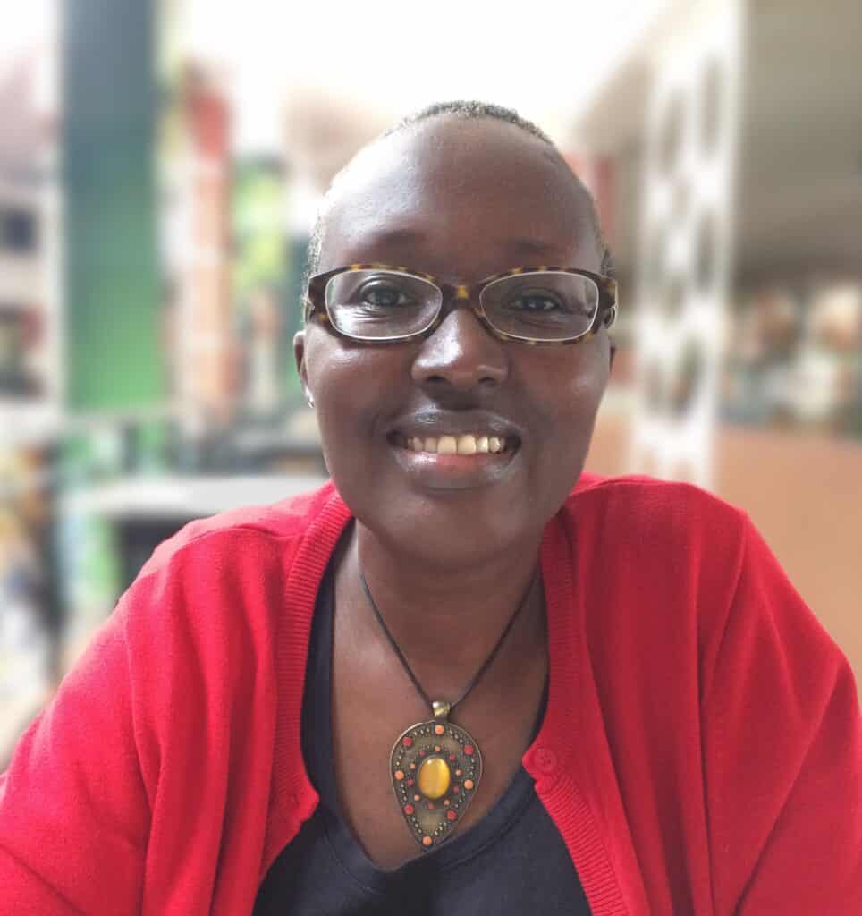Portrait of a smiling person wearing red cardigan and glasses in a bright setting.