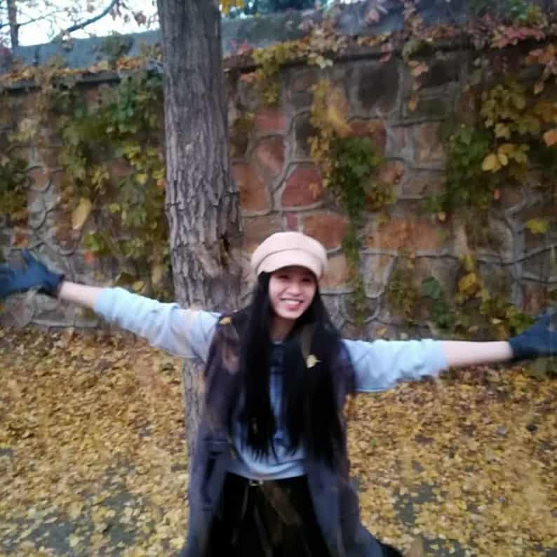 Young woman outdoors with arms outstretched in autumn setting, smiling.