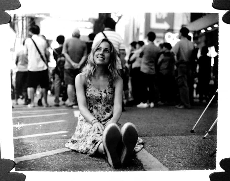 Young woman sitting on street at a busy event.