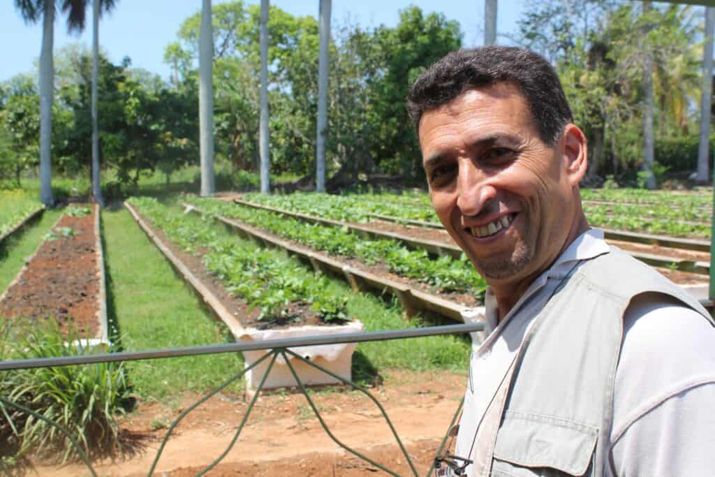 Smiling man in a garden with raised beds and irrigation pipes.