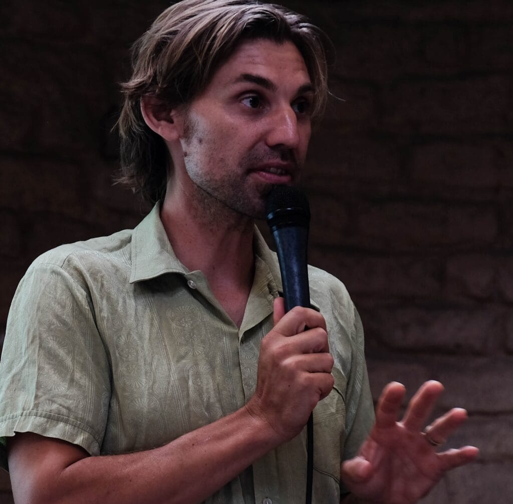 Speaker with microphone discussing sustainable communities at a Global Ecovillage Network event.