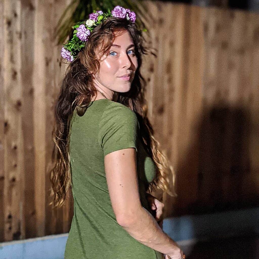 Woman with floral crown outdoors, greenery, eco village setting.