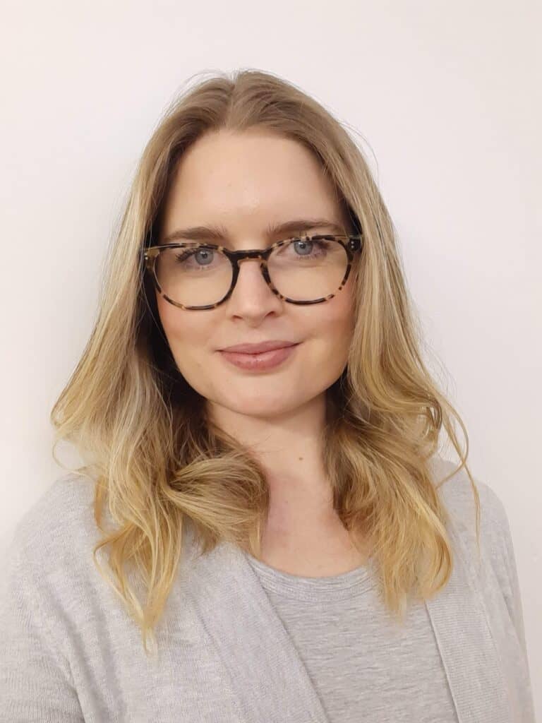 Portrait of a woman with glasses, blonde hair and a light grey top.