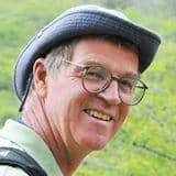 Smiling man wearing glasses and cap outdoors.